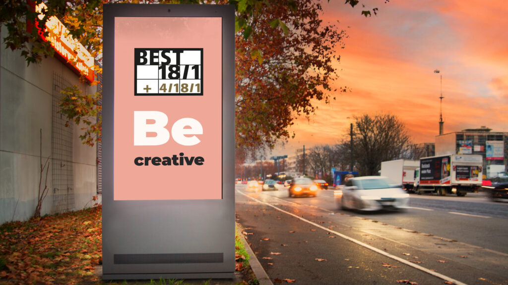 Ein digitales Citylight Poster (DCLP) am Straßenrand zeigt den Schriftzug „Be creative“ auf rosa Hintergrund. Autos und Lastwagen fahren auf der Straße vorbei, während der Himmel in warmen Orange- und Rottönen leuchtet. Herbstlaub hängt an den Bäumen entlang des Gehwegs.
