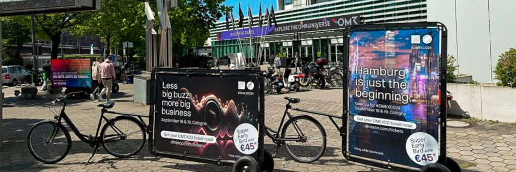 Mehrere INOVISCO CoolLiteBike stehen vor einem Messegebäude, direkt im Eingangsbereich. Die Werbeflächen auf den Fahrrädern sind auffällig gestaltet und sprechen die vorbeigehenden Besucher:innen direkt an.