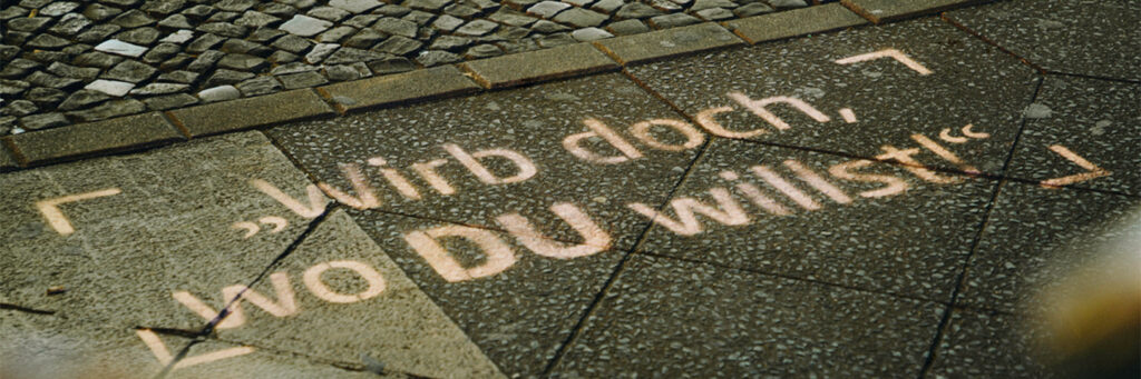 Ein INOVISCO KreideStencil zeigt auf dem Gehweg die leuchtende Botschaft „Wirb doch, wo DU willst!“. Die Botschaft fällt Passanten direkt ins Auge und sorgt für hohe Aufmerksamkeit im Straßenraum.