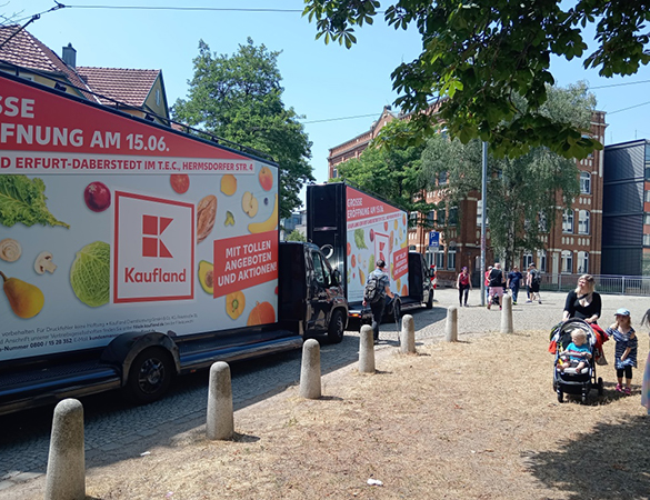 Zwei CoolLiteTruck von INOVISCO mit großflächiger Kaufland-Werbung stehen in einer belebten Straße. Die Motive bewerben die Neueröffnung einer Filiale mit Angeboten und Aktionen. Passanten und Familien mit Kinderwagen gehen im Vordergrund vorbei.