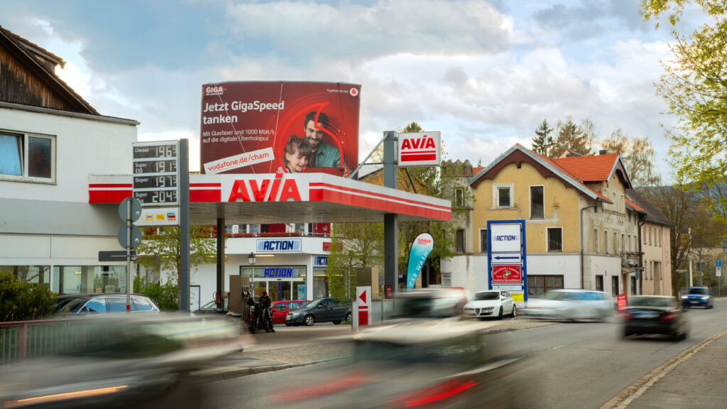 An einer gut befahrenen Straße in einer Ortschaft ist ein INOVISCO StationLight auf einem Tankstellendach platziert.