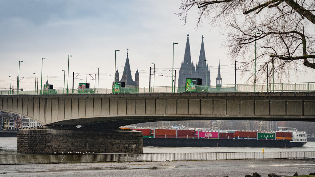 Auf dem Foto zu sehen sind drei INOVISCO CoolLiteTrucks, die hintereinander auf einer Brücke den Rhein in Köln überqueeren. Im Hintergrund ist der Kölner Dom zu sehen. Das Foto ist aus einer größeren Distanz aufgenommen.