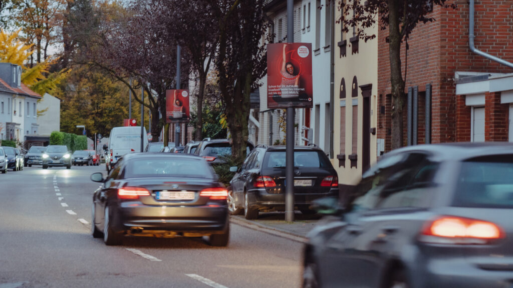 An einer befahrenen Straße in einer bewohnten Gegend, ist ein INOVISCO Hohlkammerplakat angebracht, an einer Laterne.