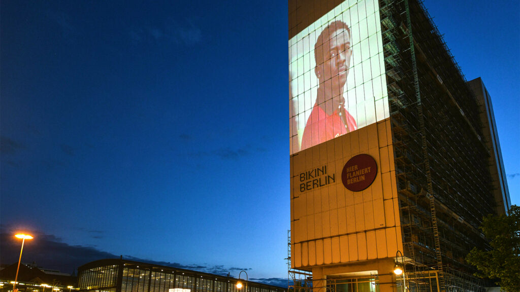 An einer großen Hausfassade ist ein Werbemotiv von "Tommy Hilfiger" mithilfe des Digitalen Riesenposters von INOVISCO projiziert.