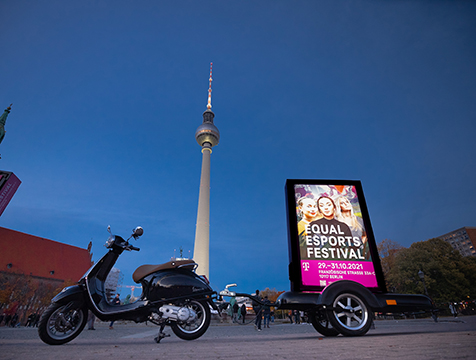 Ein INOVISCO-CoolLiteScooter steht in der Abenddämmerung auf einem großen Platz und zeigt eine Kampagne von Telekom. Der Scooter ist perspektivisch von unten fotografiert und im Hintergrund ist der Berliner Fernsehturm zu sehen.