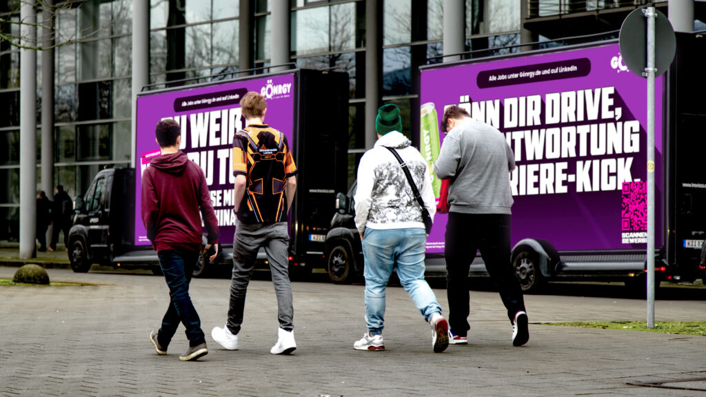 Zwei INOVISCO CoolLiteTrucks 36-1 stehen vor dem Messegelände. Davor läuft eine Gruppe von Messebesucher:innen vorbei und schaut auf eine Werbung von GÖNRGY.