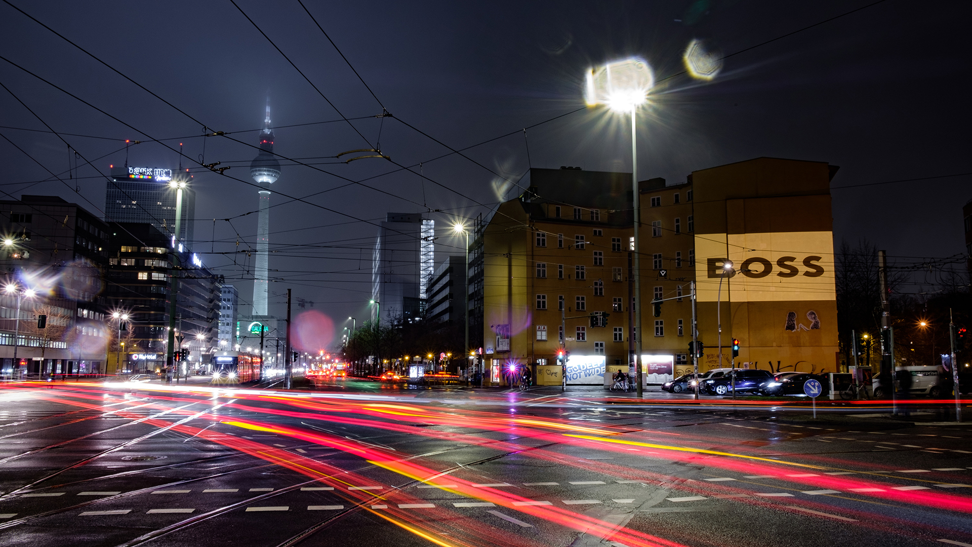 Digitales Riesenposter zu sehen an einer Berliner Straßenkreuzung, die Nachts stark befahren ist.