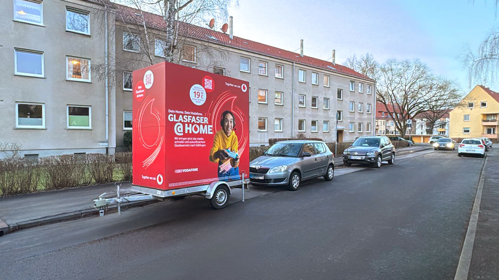 Litotrailer von INOVISCO steht mit Vodafon-Werbung am Straßenrand eines Wohngebiets.
